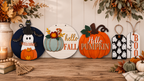 A set of four decorative autumn-themed wooden signs displayed on a rustic wooden table against a white wood-paneled wall.