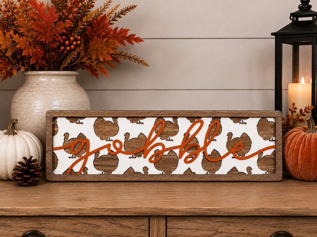 A rectangular wooden sign with a white turkey background and orange script spelling ' gobble.'