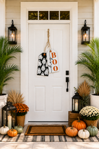 A white front door decorated for Halloween with a black and white ghost-patterned sign and a white 'hey boo' sign hanging from twine. 