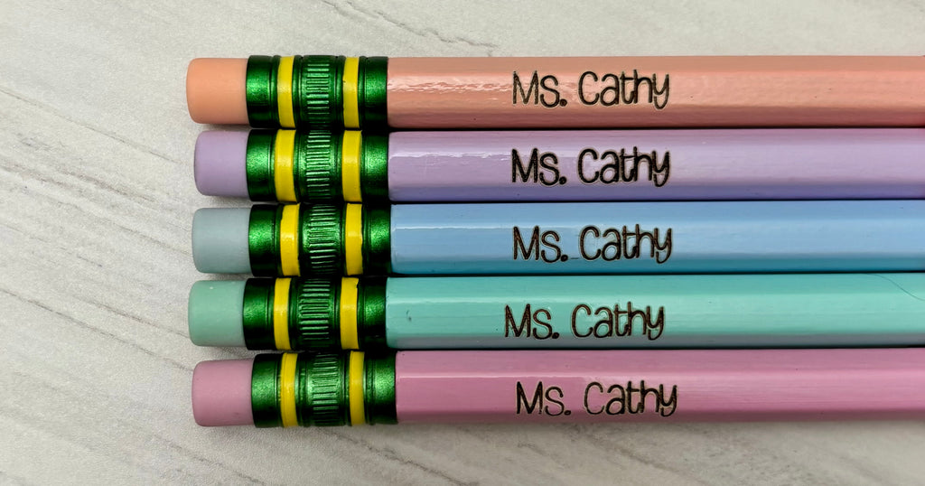 Five personalized pencils with pastel pink, purple, blue, green, and pink barrels, each engraved.