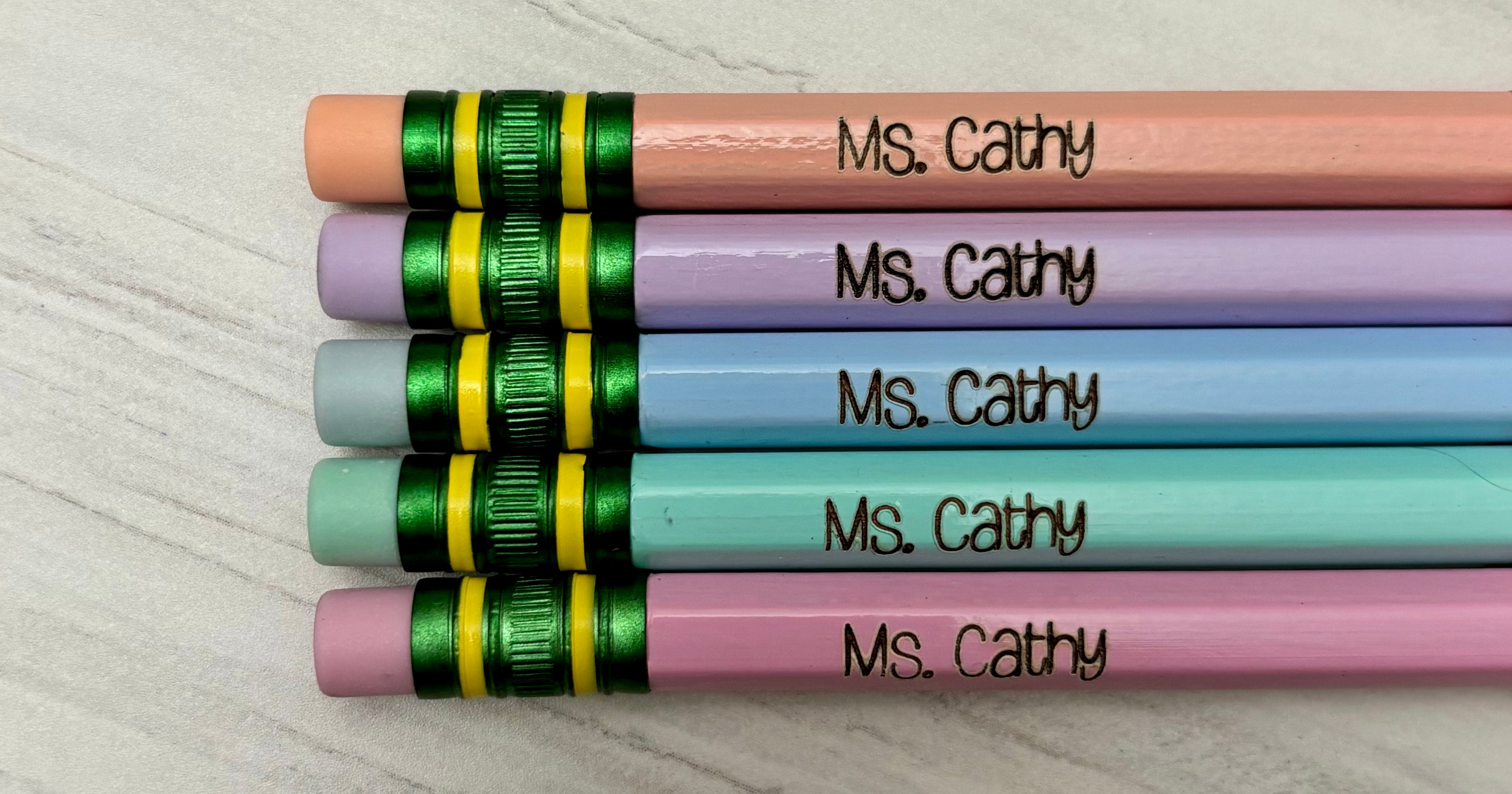 Five personalized pencils with pastel pink, purple, blue, green, and pink barrels, each engraved.