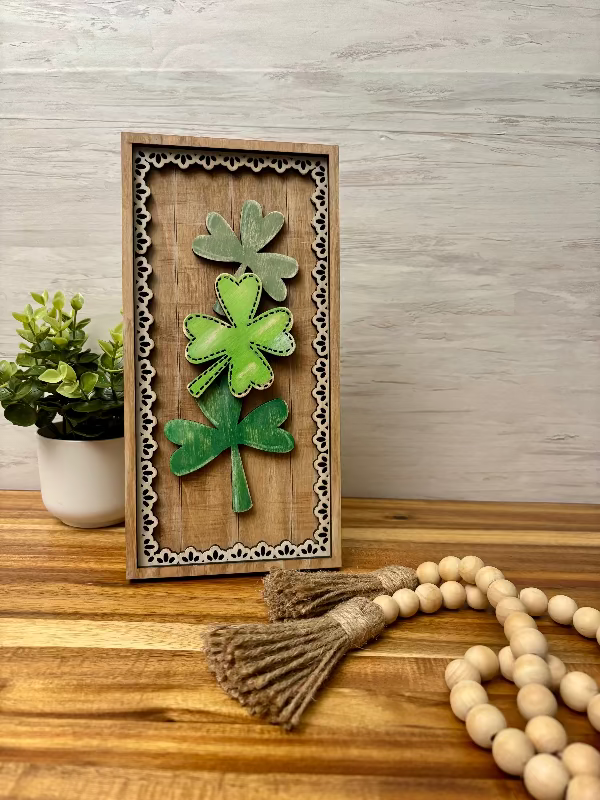 Three green shamrocks on a wood background with a wood lace frame.